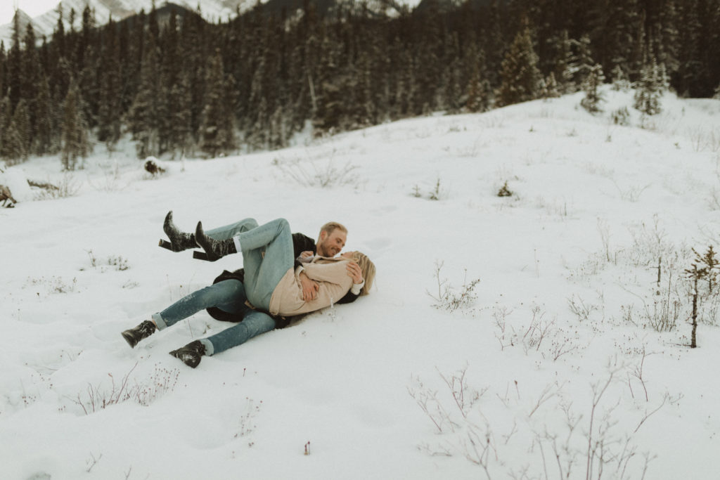 couple rolling around in the snow in the mountains