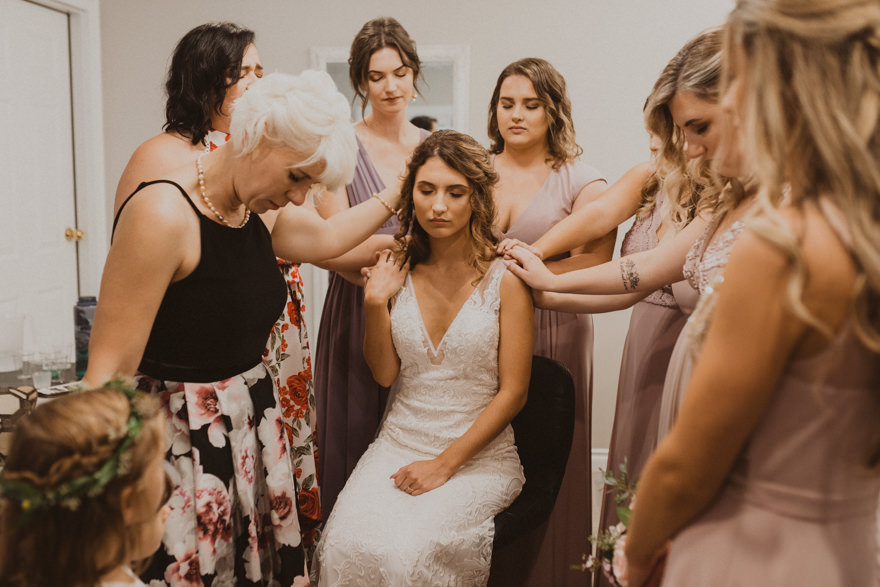 bridesmaids praying for bride while getting ready before wedding