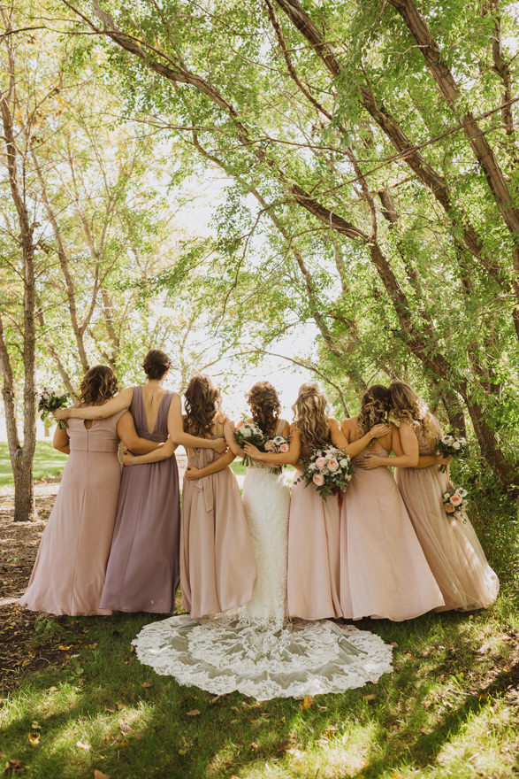 bridesmaids with arms around each other in trees in matching pink and purple dresses