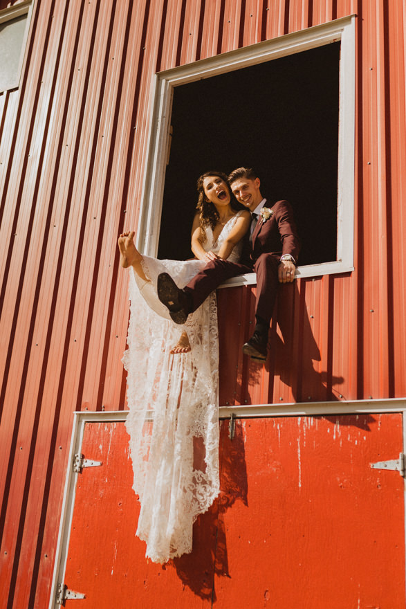 bride and groom sitting in barn doors during farm wedding in Manitoba