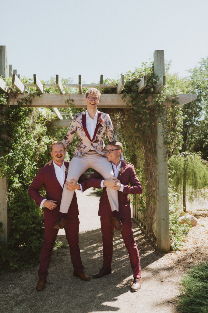 groomsmen wearing burgundy suits holding the groom in floral suit