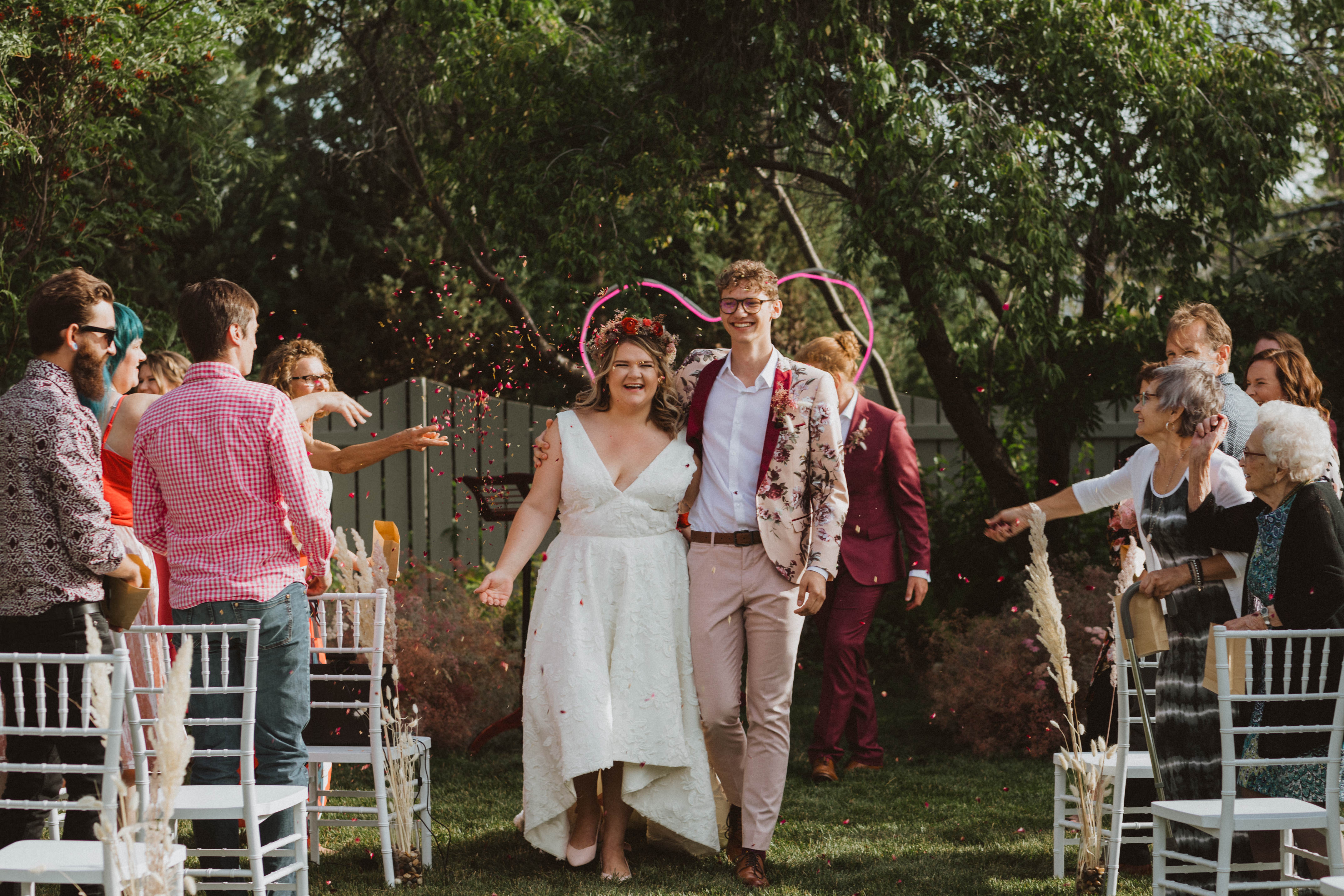 Groom in floral suit from asos, bride in BHLDN dress from Blush and Raven YYC holding colourful bouquet and wearing a flower crown of dried flowers. Intimate backyard covid wedding