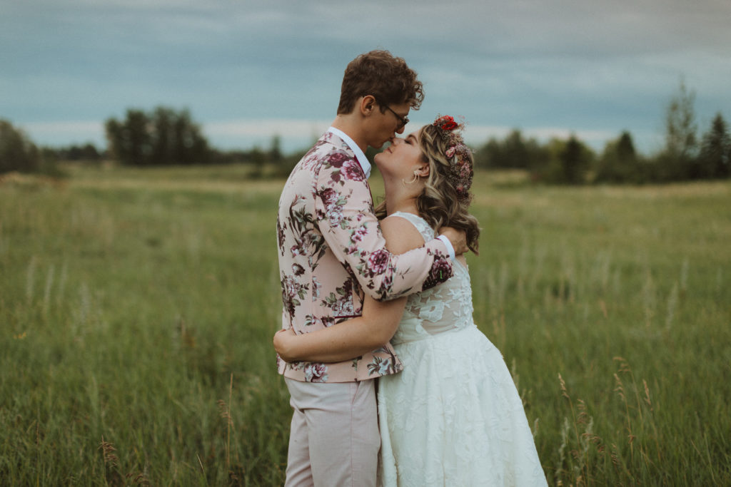 groom in floral suit from asos, bride in BHLDN dress from Blush and Raven YYC holding colourful bouquet and wearing a flower crown of dried flowers