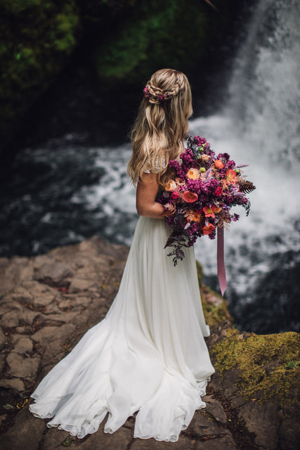 Fabloomosity Floral Atelier is an elopement florist in Edmonton and was chosen as one of Alberta's top elopement vendors. Bride seen holding a big colourful bouquet in front of a waterfall.