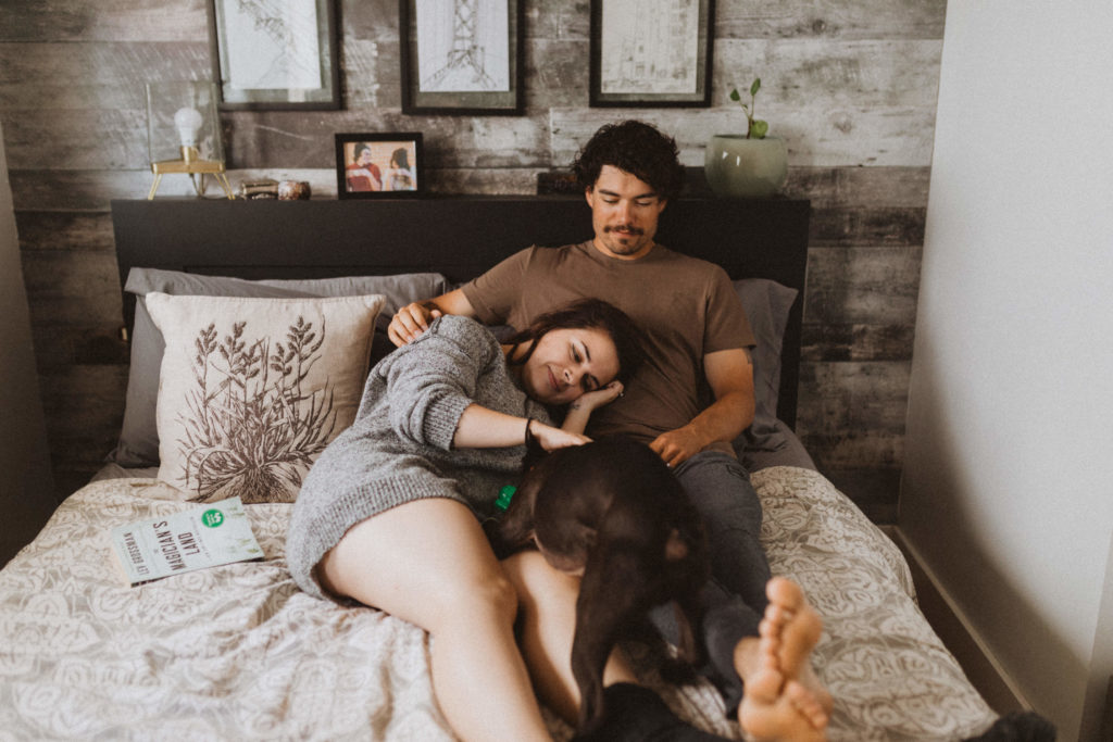 cozy in-home session, couple snuggling in bed with their dog