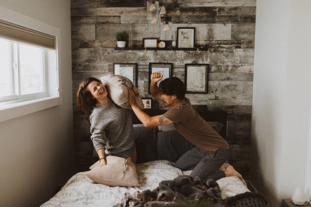 couple having a pillow fight on their bed during their in home photoshoot