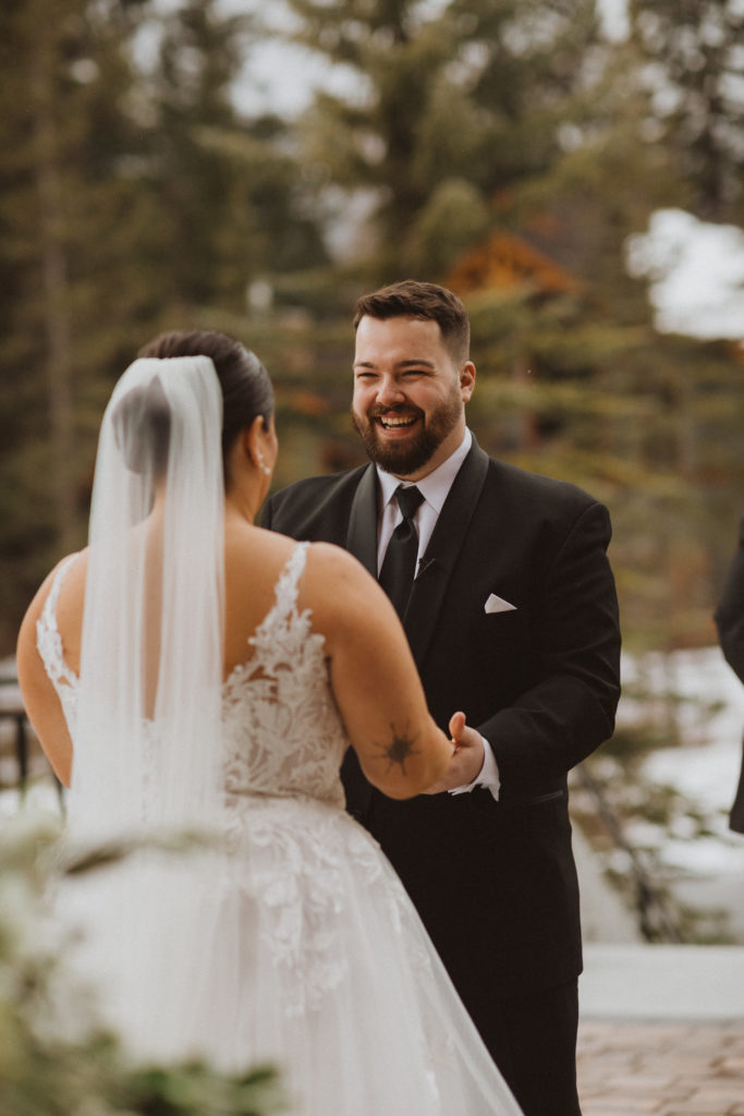 Elopement ceremony image of groom looking at bride holding hands. Ceremony in Canmore, Alberta at the Malcolm Hotel.