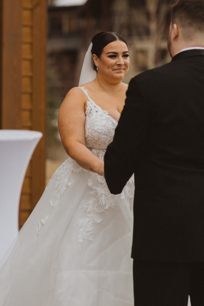 Bride and Groom holding hands during ceremony. Photo of the bride emotionally looking at her groom all dressed up in a black suit.