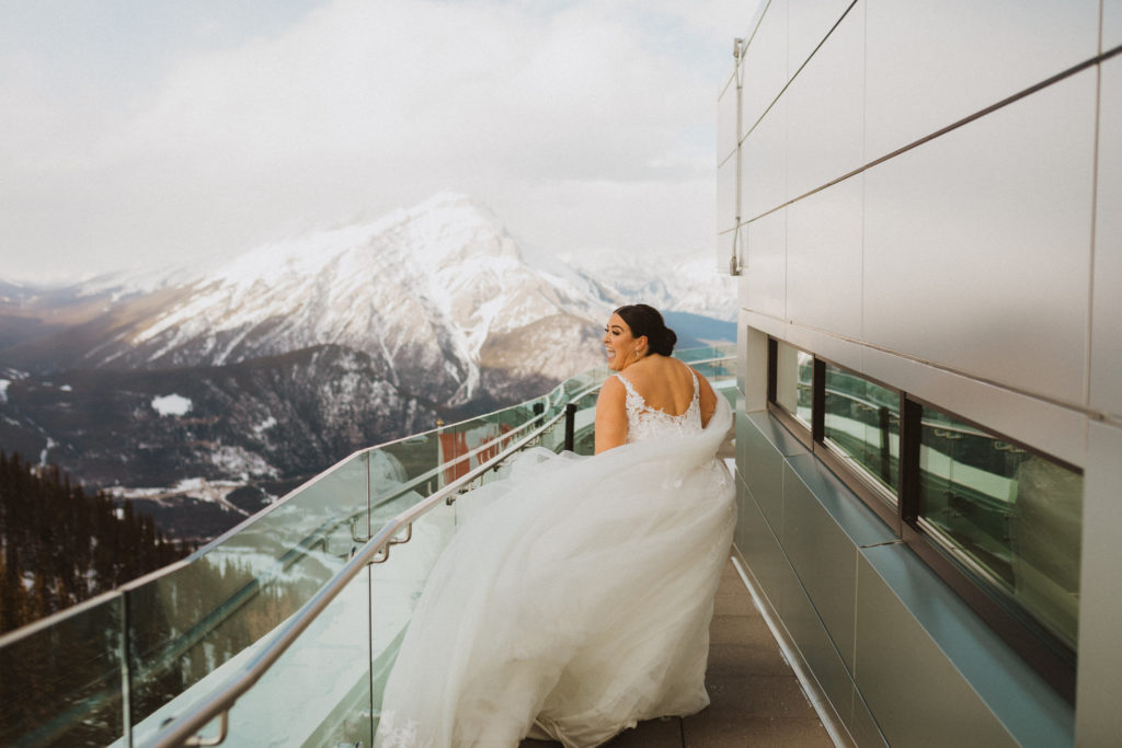 Bride running around the rooftop of the Banff Gondola lookout. Very windy and dress blowing but the bride is very happy and smiling in this portrait.