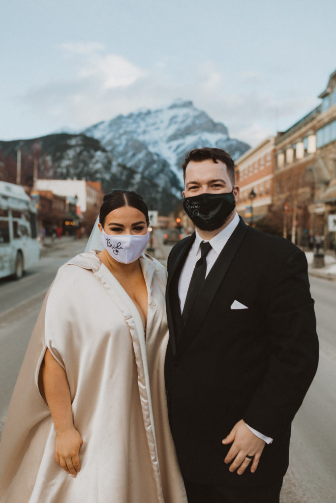 Bride and groom portrait wearing masks in the center of the town of Banff because they got eloped during corona virus, a worldwide pandemic that did not cancel love.