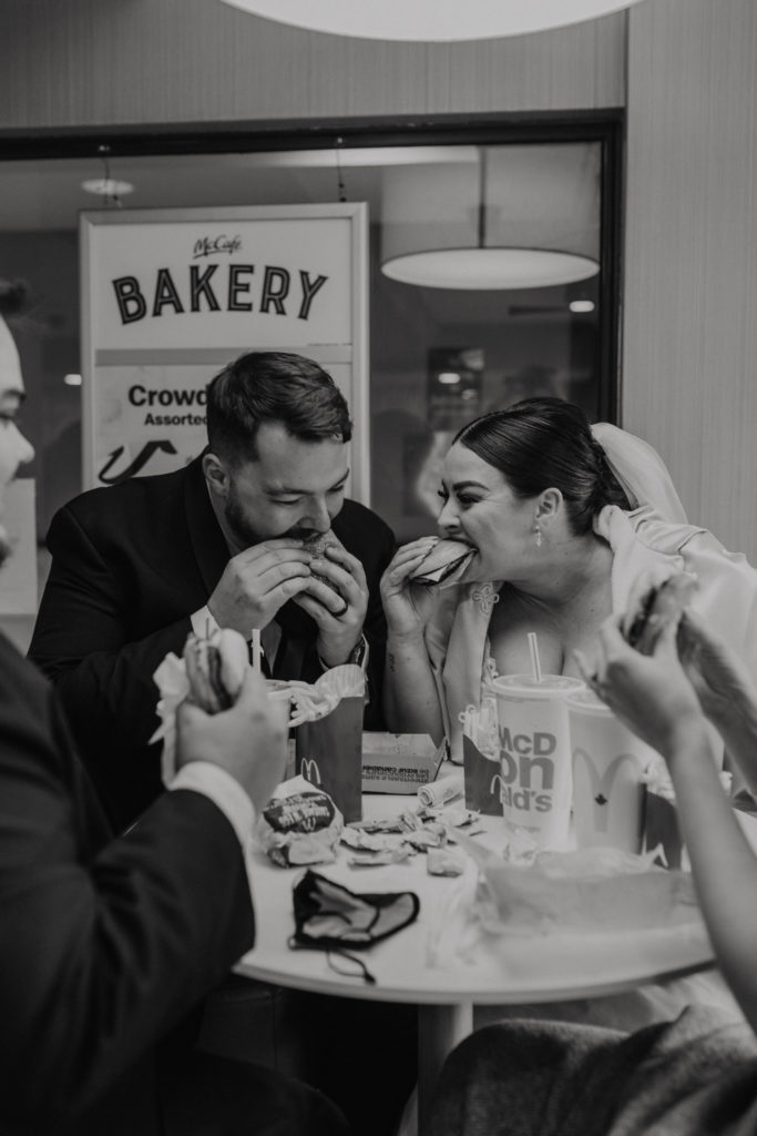 Black and white elopement photography. Bride and groom eating a Big Mac, fries, and a coke on elopement day at McDonalds as their celebratory meal.