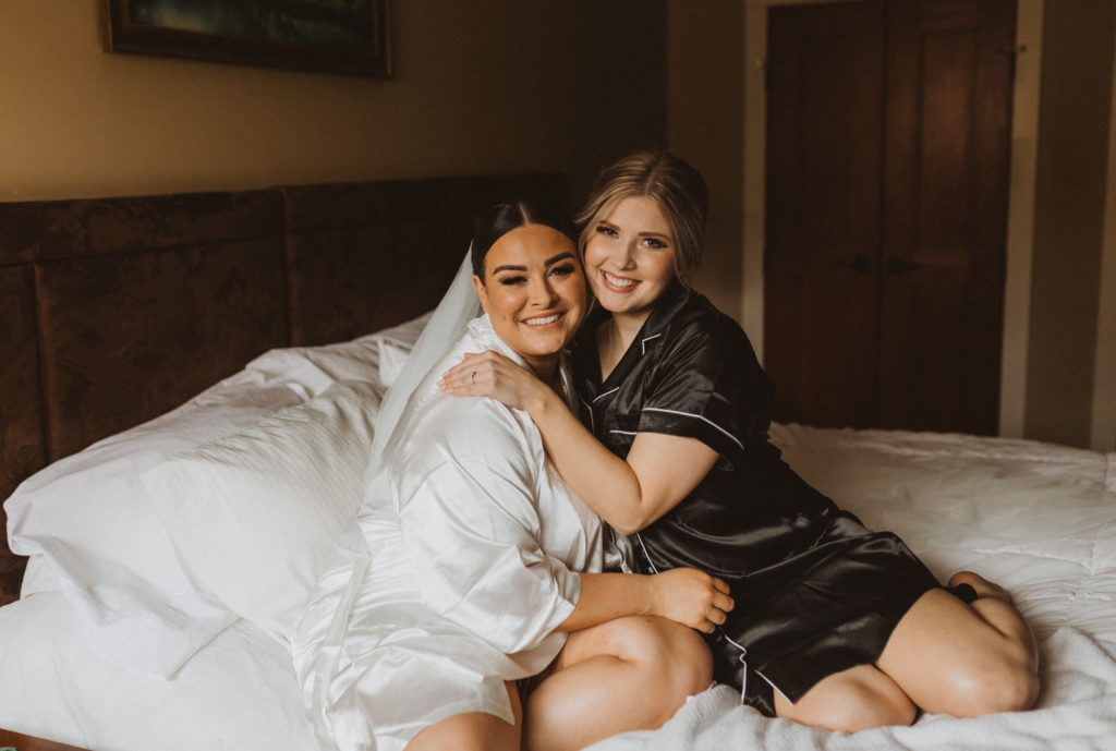Bride and maid of honour portrait cuddling on the bed while getting ready for elopement.