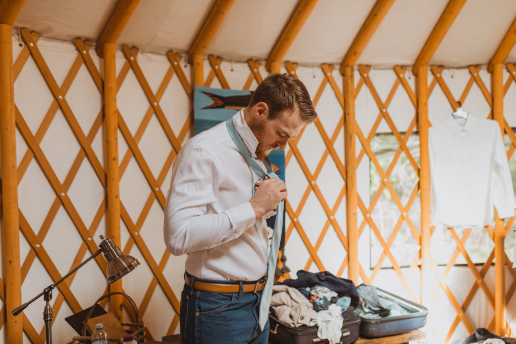 Groom getting ready for elopement day inside a yurt for his flora bora elopement. Tying his tie. Getting ready photos. Saskatchewan yurt elopement.