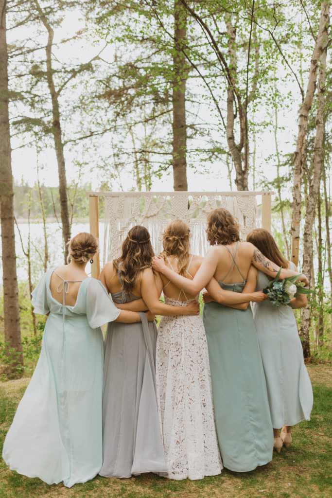 Bridesmaids back of dresses and hairstyles. Flora Bora Yurt Elopement. Wedding party portraits. Bridesmaids wearing mismatched blue bridesmaid dresses with bride in a lace wedding dress from Lulus. Groomsmen wore jeans, cowboy boots, and suspenders from Lamlees. Saskatchewan elopement photographer. Creative bridal party photo ideas.
