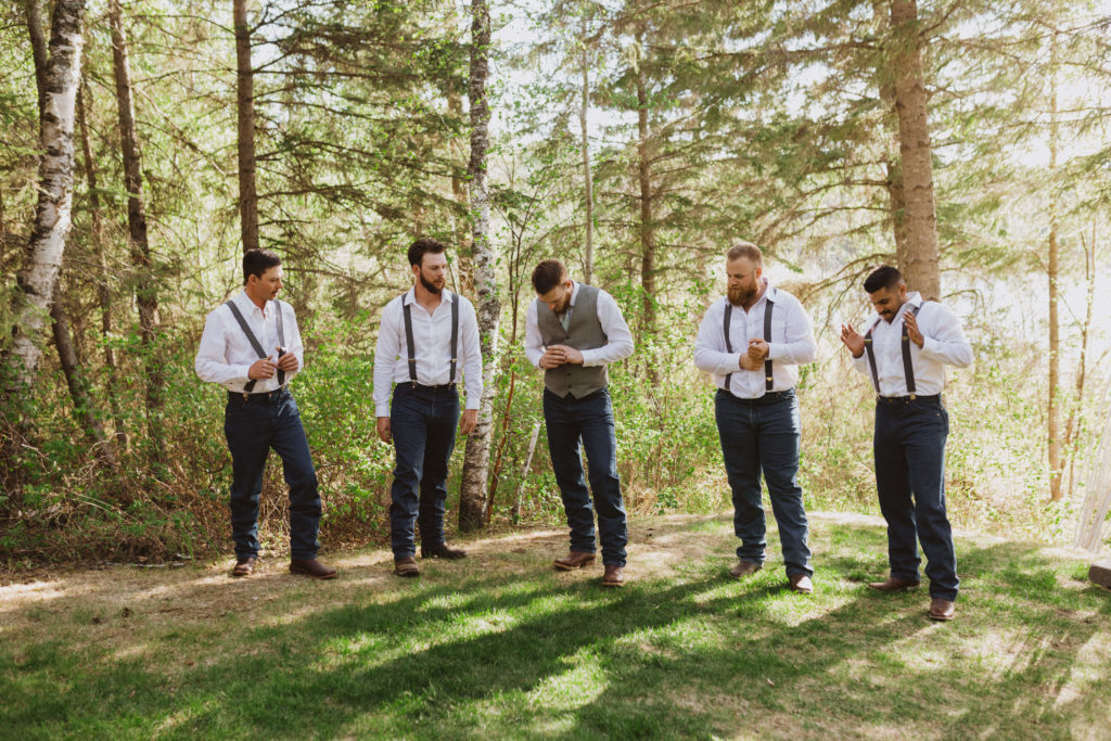 Groomsmen poses for group portraits. Flora Bora Yurt Elopement. Wedding party portraits. Bridesmaids wearing mismatched blue bridesmaid dresses with bride in a lace wedding dress from Lulus. Groomsmen wore jeans, cowboy boots, and suspenders from Lamlees. Saskatchewan elopement photographer. Creative bridal party photo ideas.