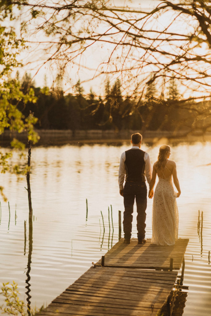 Flora Bora yurt elopement in the forest. Bride and Groom wedding portraits. Posing ideas. Couple photos by Liv Hettinga Photography a Saskatchewan elopement photographer. Sunset portraits standing on the dock looking out over the lake.
