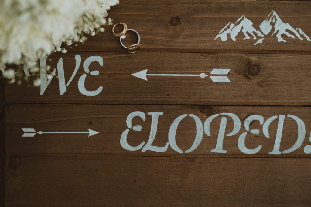 The newlyweds rings on their 'we eloped' sign at this couple's Alberta cabin elopement.