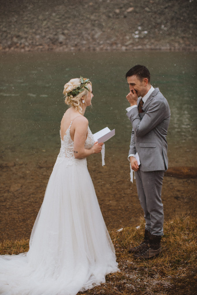 couple reads their vows in front of a glacier lake as the snow falls around them