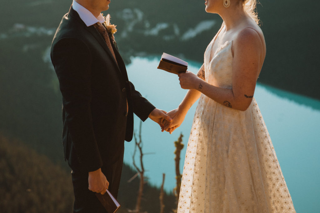 couple reading their vows overlooking Lake Louise, holding leather vow books