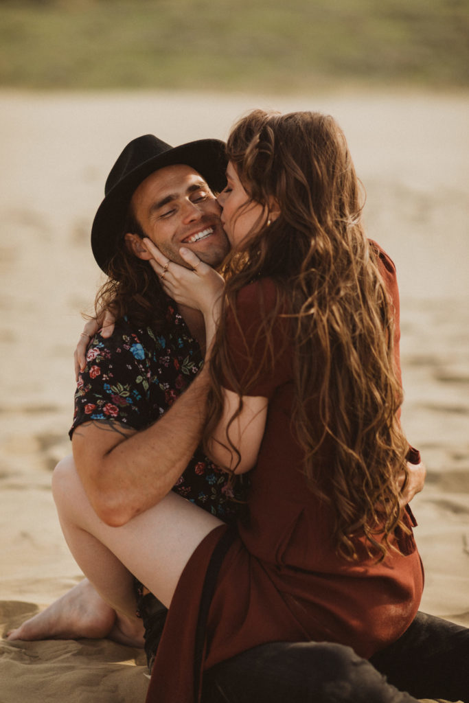 couple sitting straddle in the sand dunes for a photoshoot