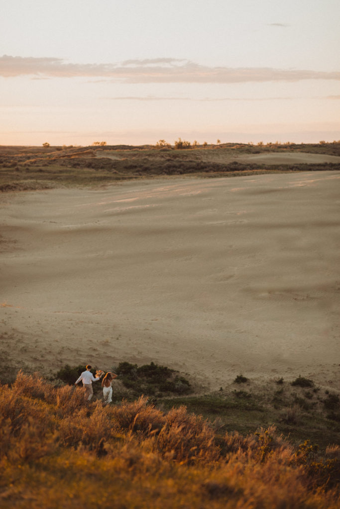 bride and groom running down hill at golden hour into the sand dunes at golden hour