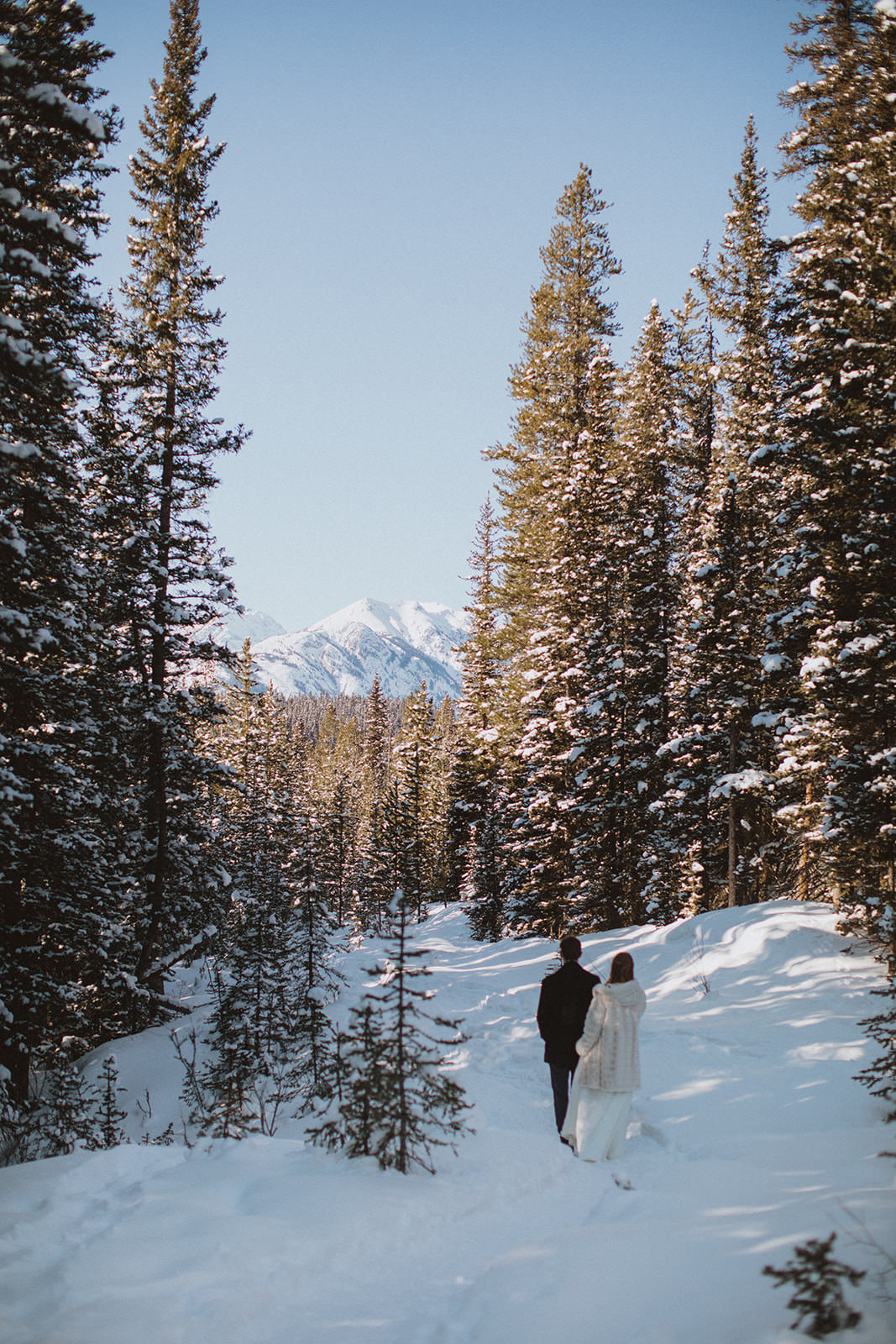 bride and groom go hiking on their elopement day through the snow